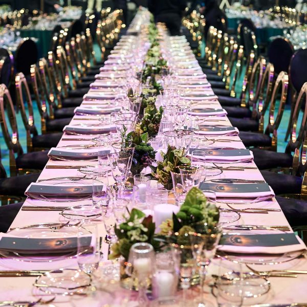 Lange festlich gedeckte Tafel mit Blütenzentren, Kerzen, Gläsern und Besteck; goldene Stühle säumen beide Seiten.