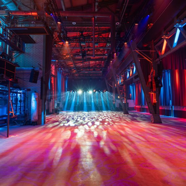 Leerer Veranstaltungsraum mit bunten Lichtstrahlen und Bühne.